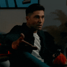 a man in a black jacket is sitting on a couch holding a game controller .