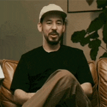 a man wearing a hat and a black shirt is sitting in a chair