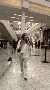 a woman in a white shirt is walking down an escalator in a shopping mall