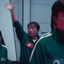a man in a green uniform with a red x on his chest raises his hand .