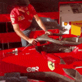 a man in a red ferrari shirt is working on a red race car