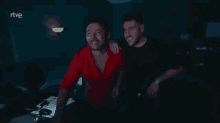 two men are posing for a picture in a dark room with the rtve logo in the background