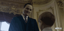 a man in a suit and tie talks to a young boy in a room with a netflix logo in the corner