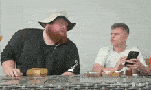 a man with a beard wearing a hat is sitting at a table with another man .
