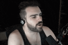 a man with a beard is singing into a microphone while wearing headphones and a tank top .