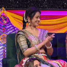 a woman in a traditional indian dress is sitting on a couch applauding .