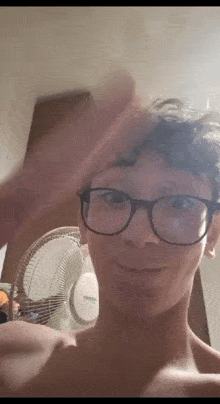 a young man wearing glasses is taking a picture of himself in front of a fan .