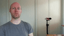 a man in a gray shirt stands in front of a microphone