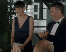 a woman in a blue dress stands next to a man in a tuxedo holding a glass of wine .
