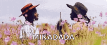 a couple of people standing in a field of flowers with the word mikadada on the bottom .