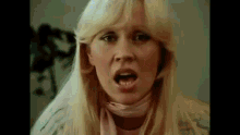 a woman with long blonde hair and a pink scarf around her neck is making a funny face .