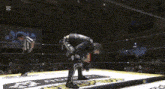a man is kneeling down in a wrestling ring while a referee stands behind him .