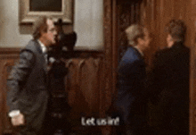 a group of men in suits are standing next to each other in a room and one of them is saying let us in .