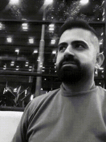 a man with a beard is looking at the camera in a black and white photo .