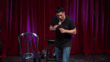 a man in a black shirt is standing in front of a red curtain holding a microphone .