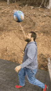 a man with a beard is balancing a globe on a stick