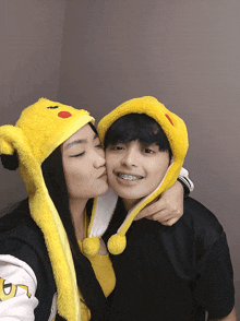 a girl is kissing a boy on the cheek while wearing a pikachu hat
