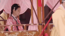 a woman in a pink dress is sitting on a balcony next to a man in a yellow dress .