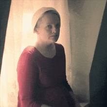 a woman wearing a red dress and a white hat looks out of a window