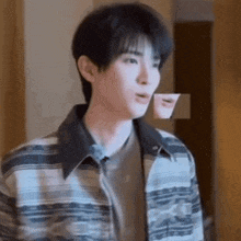 a young man wearing a plaid jacket is standing in a room .