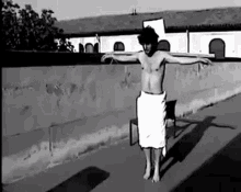a black and white photo of a shirtless man in a towel standing next to a chair .