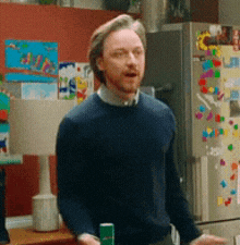 a man in a blue sweater is standing in front of a refrigerator that has a sunflower on it