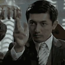 a man in a suit and tie is pointing his finger at the camera .