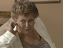 an older woman is talking on a cell phone with a white shirt that says ' embroidered sleeves ' on it