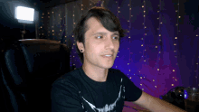 a man in a black shirt is smiling in front of a purple curtain