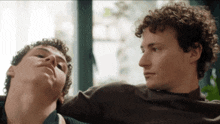 two men with curly hair are sitting next to each other on a couch