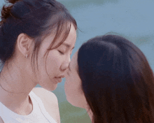 two women kissing with their eyes closed in front of a blue sky