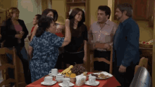 a group of people are standing around a table with plates of food on it