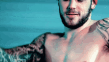 a shirtless man with a beard and tattoos on his arms .