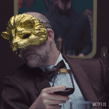 a man wearing a gold mask is holding a glass of wine with a netflix logo in the corner