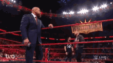 a man in a suit stands in a wrestling ring with a sign that says wrestlemania on it