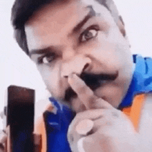 a man with a mustache is holding a cell phone in his hand and pointing at it .