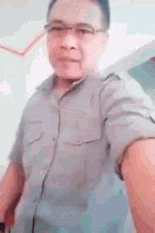 a man wearing glasses and a grey shirt is taking a picture of himself .