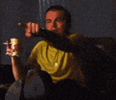 a man in a yellow shirt is sitting in a chair smoking a cigarette and drinking beer