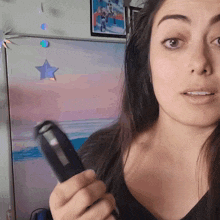 a woman is holding a remote control in front of a painting of a beach