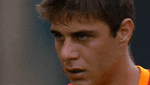 a close up of a man 's face wearing an orange shirt