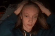 a young girl is holding her head with her hands while wearing a blue hoodie .