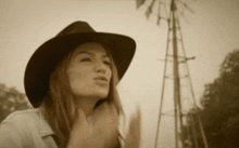 a woman wearing a cowboy hat stands in front of a windmill in a sepia tone photo