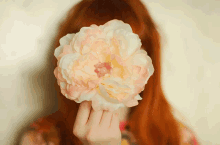 a woman with red hair is covering her face with a flower