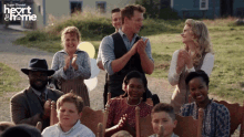 a group of people clapping in front of a sign that says heart and home