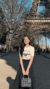 a woman wearing a christian dior t-shirt is standing in front of the eiffel tower