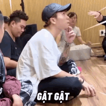 a man wearing a hat is sitting on the floor with a group of people behind him and a caption that says gat gat