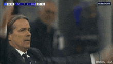 a man in a suit and tie holds his head while watching a cbs sports broadcast