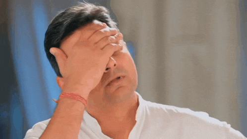 a man in a white shirt is covering his face with his hands