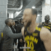 a basketball player in a golden state warriors jersey is shaking hands with a man in a suit .