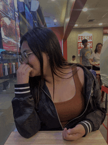 a girl sits at a table in front of a fresh fresh sign